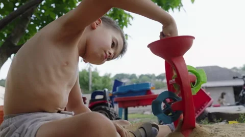 Side view of a boy putting sand in a plastic machine outside the garden stand Stock Footage 247141415