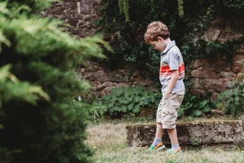Side view of boy standing in garden against stone wall Stock Photos