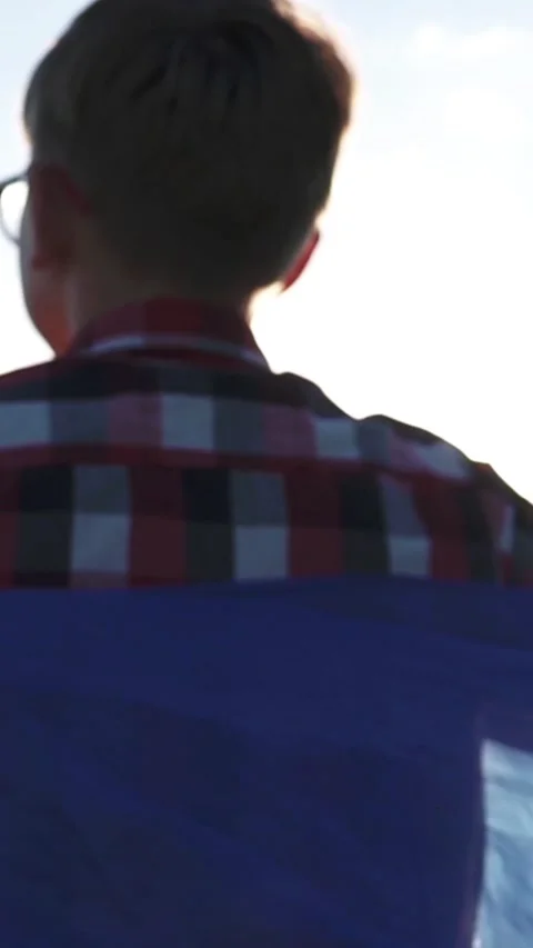 Side view of a boy with Ukrainian flag wrapped around shoulders at sunset Vídeos de archivo 337710845