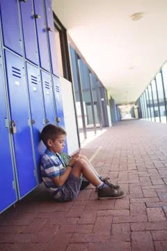 Side view of boy using mobile phone while sitting by lockers 스톡 사진