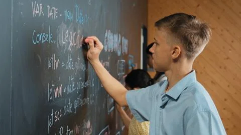 Side view of boy writing code on blackboard with diverse friend. Edification. 写真素材