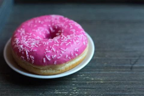Side view to bright pink donut on white round plate and aged wooden grey Stock Photos