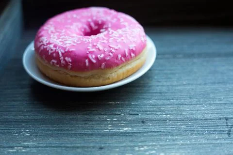Side view to bright pink donut on white round plate and aged wooden grey Foto stock