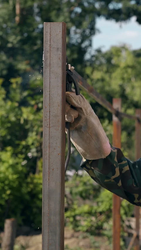 Side view builder in uniform welds house fence in yard Видео 308010869