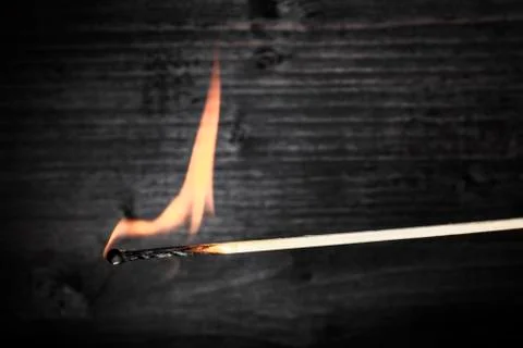 A side view of a burning match, with fire, on a dark background with a place for 写真素材
