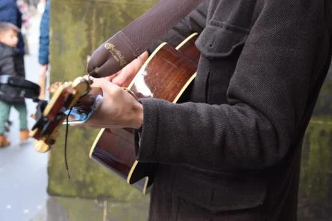 Side view of busker playing brown acoustic guitar infront of green wall Stock Photos