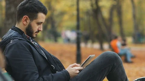 Side view calm handsome bearded man holding modern tablet pc autumn park sitting Stock Footage 81784884