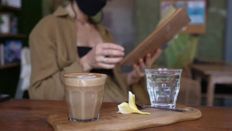 Side view of cappuccino served in a glass on a wooden tray and young woman in a Video stock 157442174