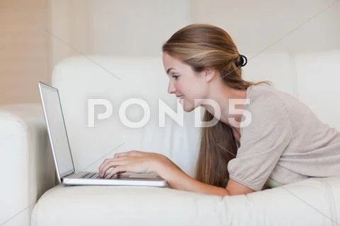 Side view of casual woman using laptop on sofa Stock Photos