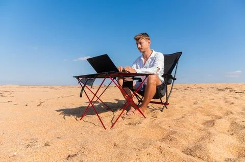 Side view of Caucasian man using laptop while sitting in sun lounger on beach on Stock Photos