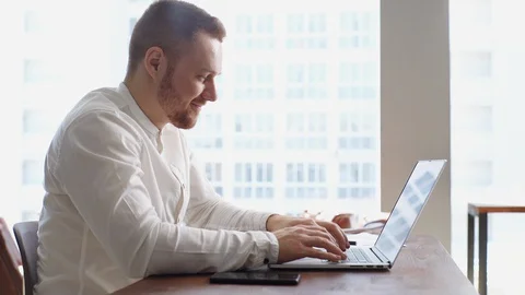 Side view of cheerful bearded young businessman working on laptop at the desk. Stock Footage 130072113