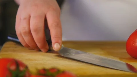 Side view chef cuts a tomato into half rings and slices on a cutting board Stock Footage 76086540