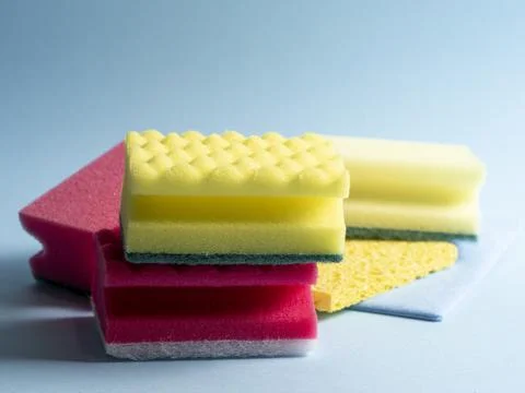 Side view of cleaning sponges of different colors and sizes laid out on a blu Stock Photos