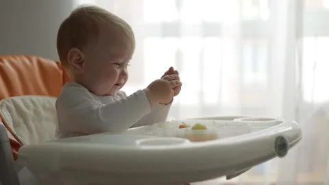 Side view. Close-up. Little boy eats baby food with his hands in a feeding chair Stock Footage 133439756