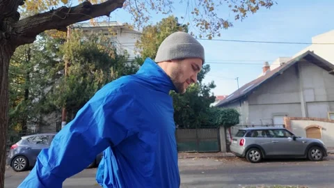 Side view close-up of a man in blue sports jacket and beanie walking on a city Stock Footage 316827585