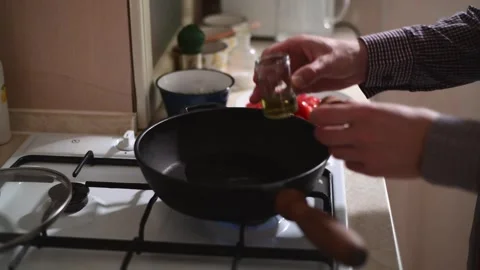 Side view close-up of a man frying cherry tomatoes in a pan 库存影片 328255756