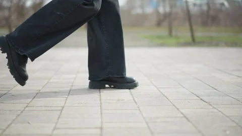 Side view close-up of person in black boots and dark jeans walking Vidéo 318629116