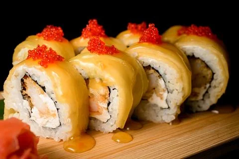 Side view close-up of sushi rolls covered in yellow sauce and topped with red Photos
