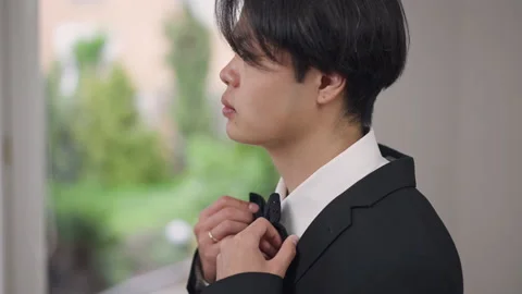 Side view close-up of young Asian man trying on bow tie indoors looking away in Stock Footage 155126612