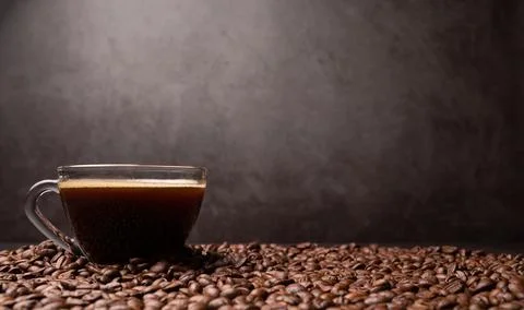 The side view of a coffee cup and group of black coffee beans is the backgrou Stock Photos