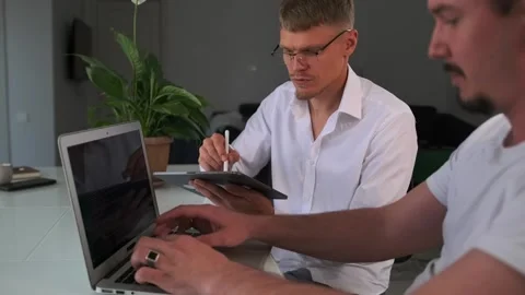 Side view. Colleagues use a laptop and tablet, collaborating and discussing. Stock Footage 299894730