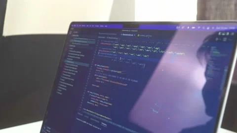 Side view of computer code scrolling back and forth on a reflective laptop Stock Footage 213798724