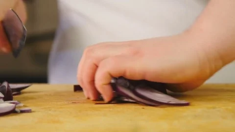 Side view cook cuts a red onion into half rings and shreds it on a wooden Stock Footage 76087063