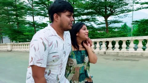 Side view of a couple walking together in a park surrounded by greenery and.. Stock Footage 262365764