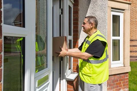 Side View of Courier Handing Over Parcel To Customer at Front Door Stock-Fotos
