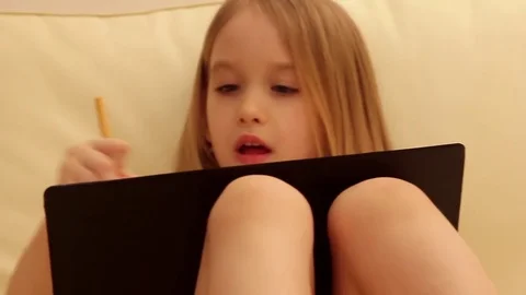 Side view of creative young girl drawing in a jotter while sitting on sofa at Stock Footage