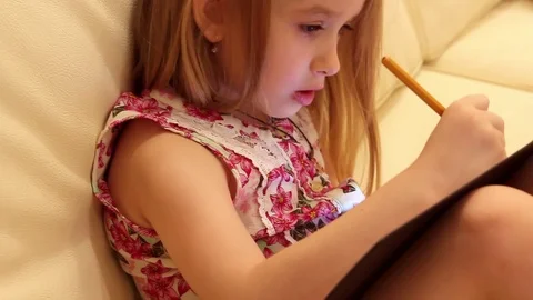 Side view of creative young girl drawing in a jotter while sitting on sofa at Stock Footage