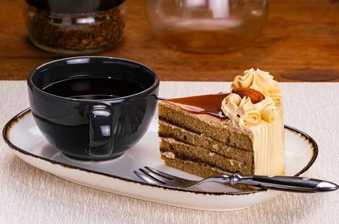 Side view of a cup of black coffee and a slice of coffee layered cake. Stock Photos
