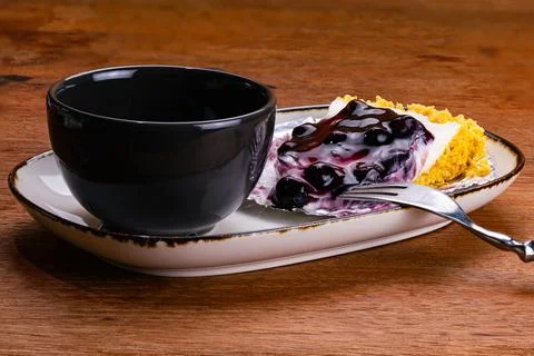Side view of a cup of coffee in black ceramic cup with blueberry cheese pie. Foto stock