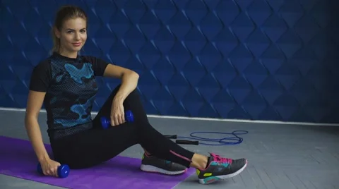 Side view of cute blonde trainer posing on fitness mat with dumbbells in modern Stock Footage 65381643