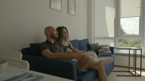 Side view of cute couple sitting on sofa and watching TV. Man switches channels. Stock Footage 167367343