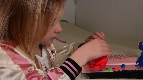 Side view of a cute fair-haired little girl making plasticine man in her room Stock-Footage 127703013