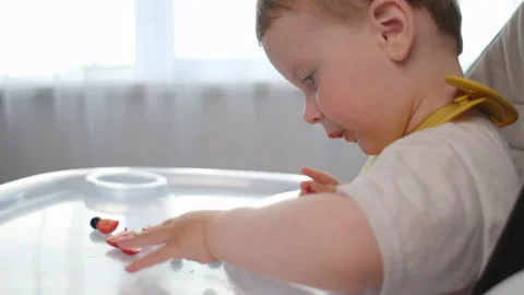 Side view of cute little boy in high chair eats fresh strawberries and blueberry Stock Footage 280177660