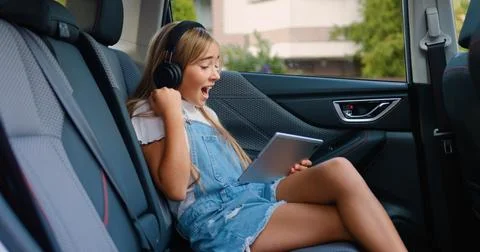 Side view of cute satisfied cheerful teen girl in earphones which sitting in the Stock Photos