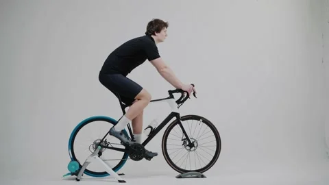 Side view of a cyclist training on an exercise bike in bright white studio Vídeo Stock 171116968