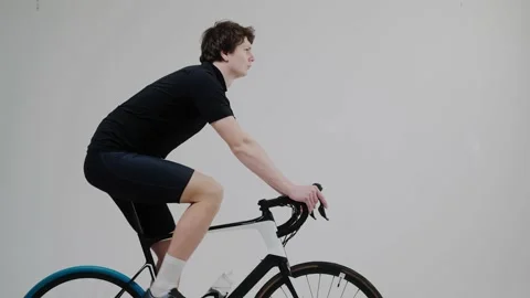 Side view of a cyclist training on an exercise bike in bright white studio Vídeo Stock 171117848