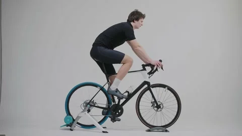 Side view of a cyclist training on an exercise bike in bright white studio 스톡 동영상 171118821