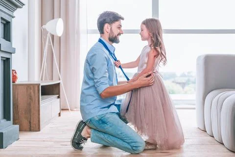 Side view of daughter tying tie on her father standing face to face in living Stock Photos