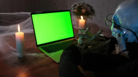 Side view death skeleton rubbing bone hands sitting at laptop with chromakey Stockbeeldmateriaal 249640600