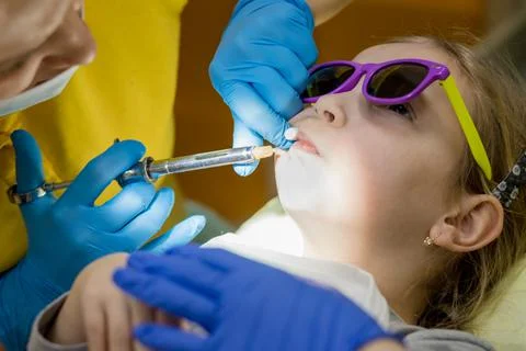 Side view of dentist holding a syringe and anesthetizing her little girl patient Stock Photos