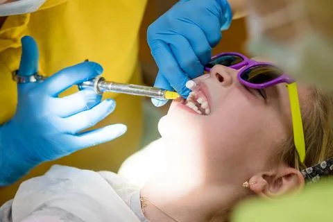 Side view of dentist holding a syringe and anesthetizing her little girl patient Stock Photos