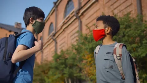 Side view of diverse schoolboys in protective mask doing elbow greeting outdoors Stock Footage 141926530