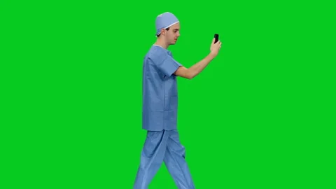 Side view of doctor in uniform having a videochat while walking on green screen Stock Footage 126514334
