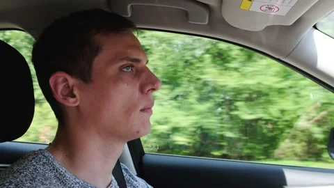 Side view of the driver. Young man driving a moving car, trees flickering Video stock 145988618