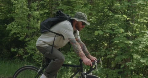 Side view of eco cyclist riding through forest - camera drifting back Stock Footage 312354760