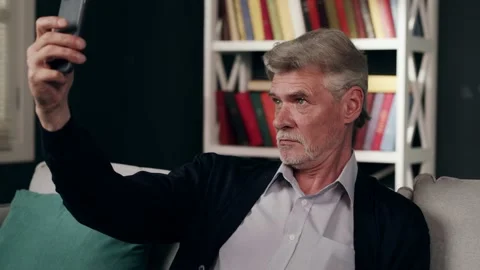 A side view of an elderly grey-haired man taking selfie with the mobile phone Видео 132667721